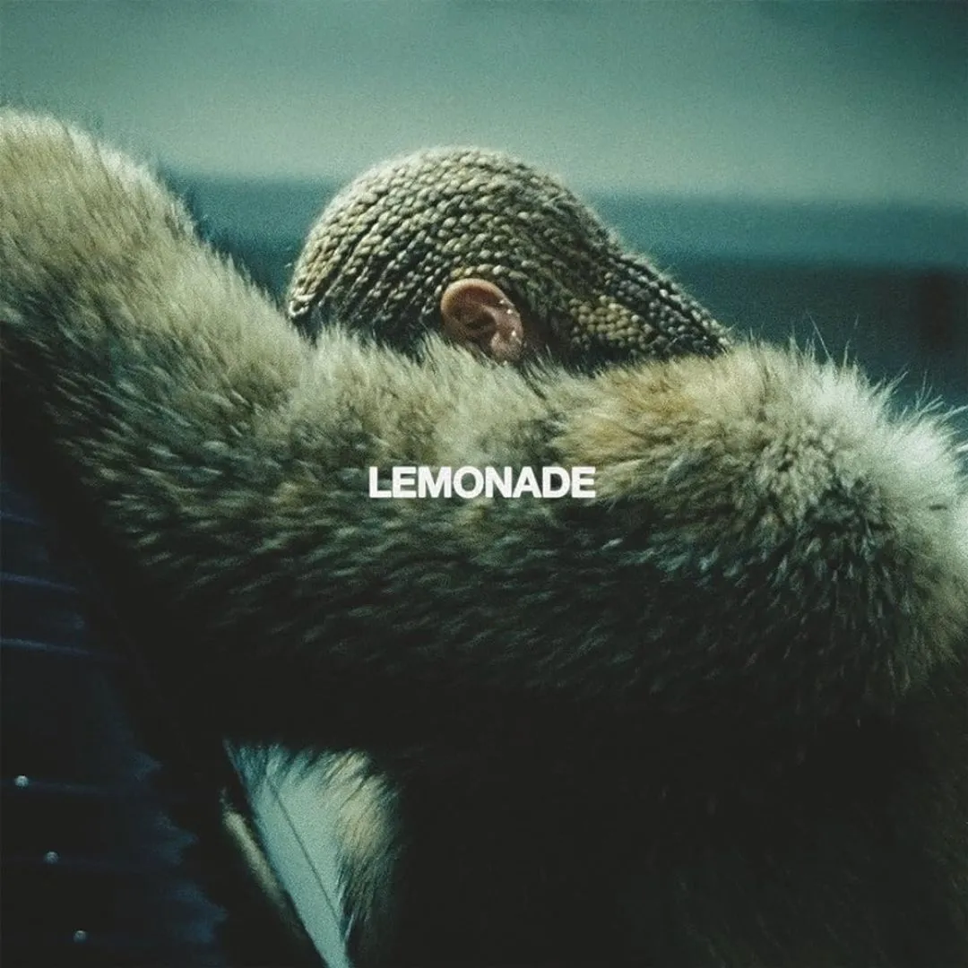 Beyoncé leaning over a car in a big fur coat and while donning braids. her face hidden. 