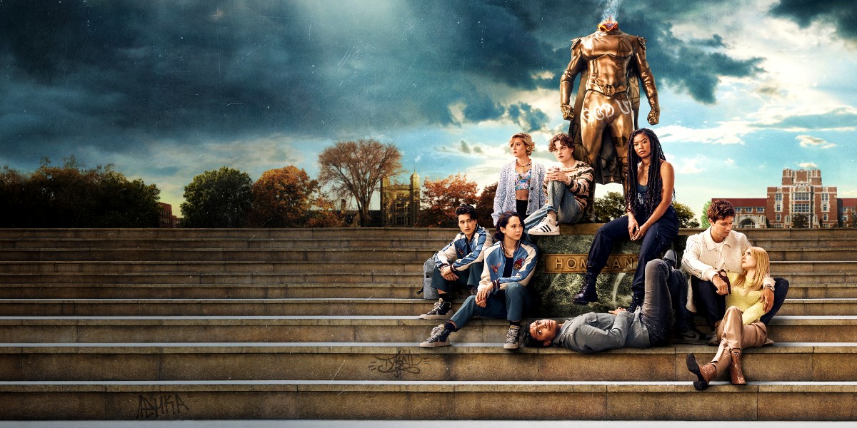 The cast of Gen V next to a headless Homelander statue