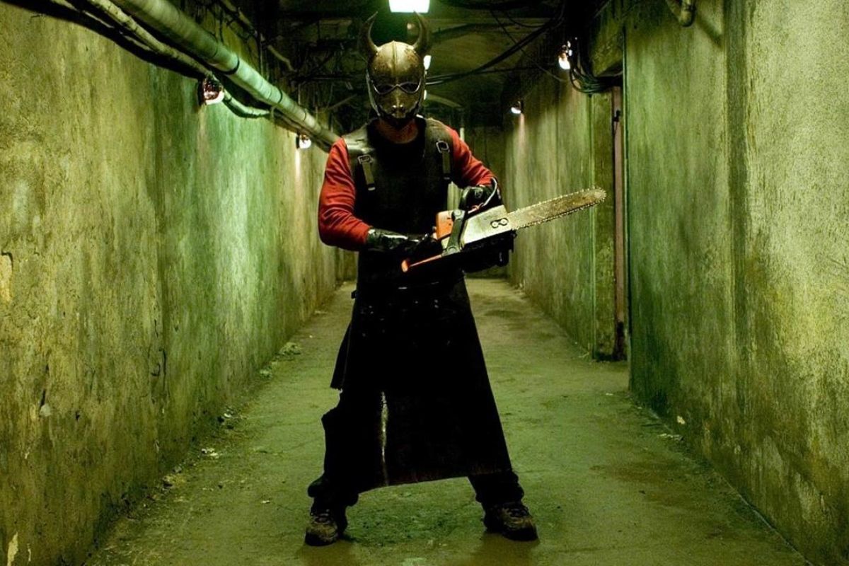 A masked man wielding a chainsaw in a creepy hallway in 'Hostel'