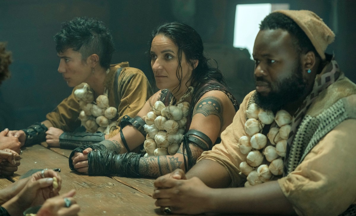 Three people sit at a table wearing garlic necklaces in 'Our Flag Means Death.'