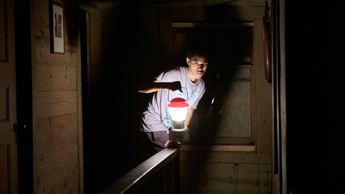 A young man (Kelvin Harrison Jr.) investigates a dark cabin with a lantern in 'It Comes at Night'