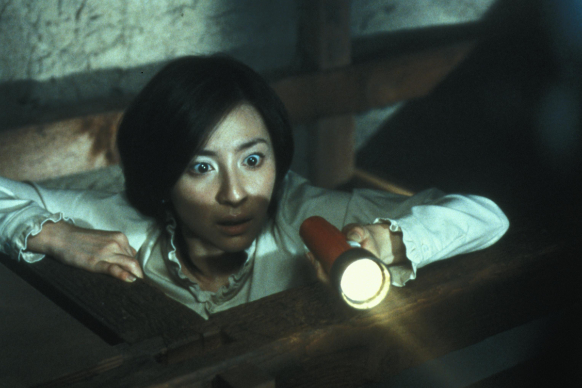 A woman looks startled while holding a flashlight in the dark in 'Ju-On: The Grudge'