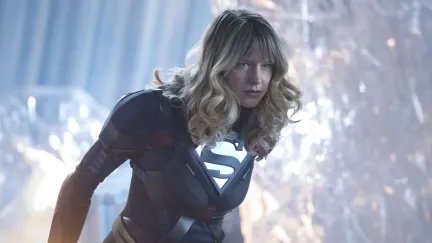 Image of Melissa Benoist as Kara Zor El in the CW's 'Supergirl.' She is dressed ni a black Supergirl suit and standing in the Fortress of solitude. She is a young white woman with long blonde hair and bangs. She is leaned forward about to angrily attack.