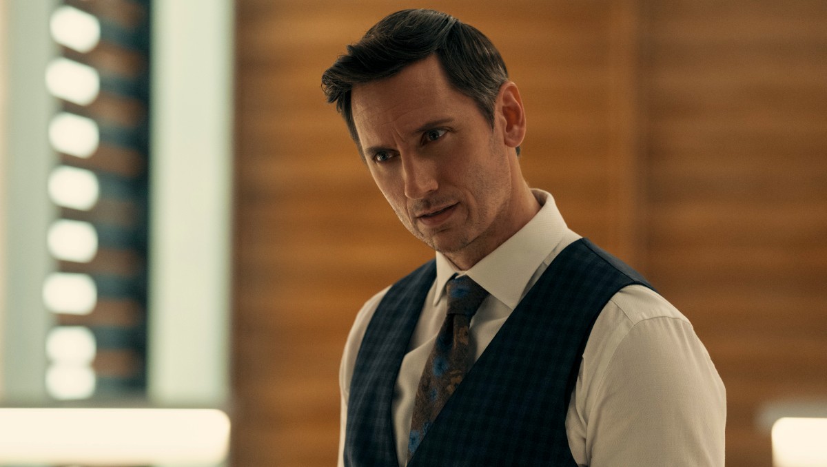 A man wears a suit and tilts his head to the side while focusing in 'Gen V'.