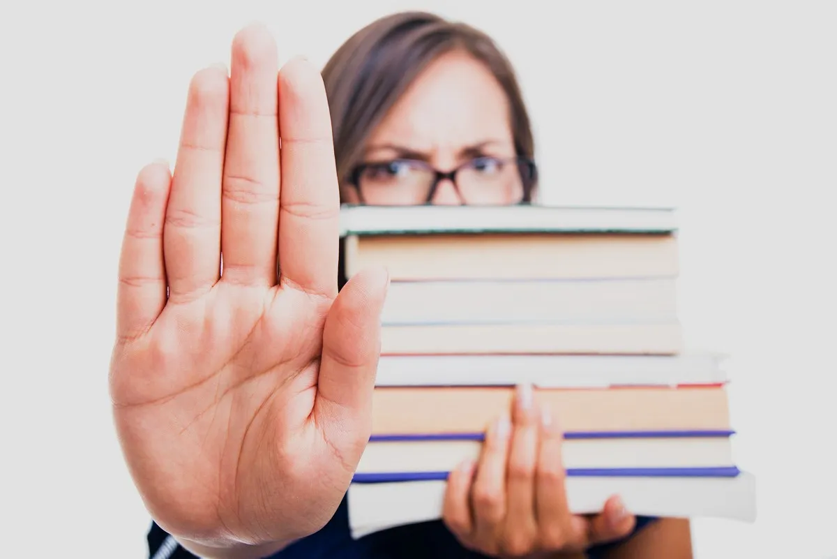 Woman holding a stack of books while gesturing "stop"