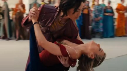 Prince Yan dips Carol Danvers as they dance. Carol is wearing a red dress with her iconic gold star on the chest.