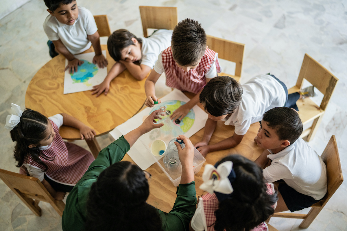 Teacher talking to students about recycling, seen from above in a classroom.