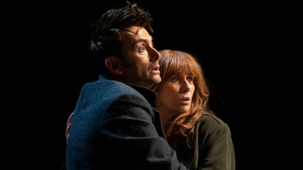 The 14th Doctor clutches Donna Noble against a black background. They're looking up at something frightening.