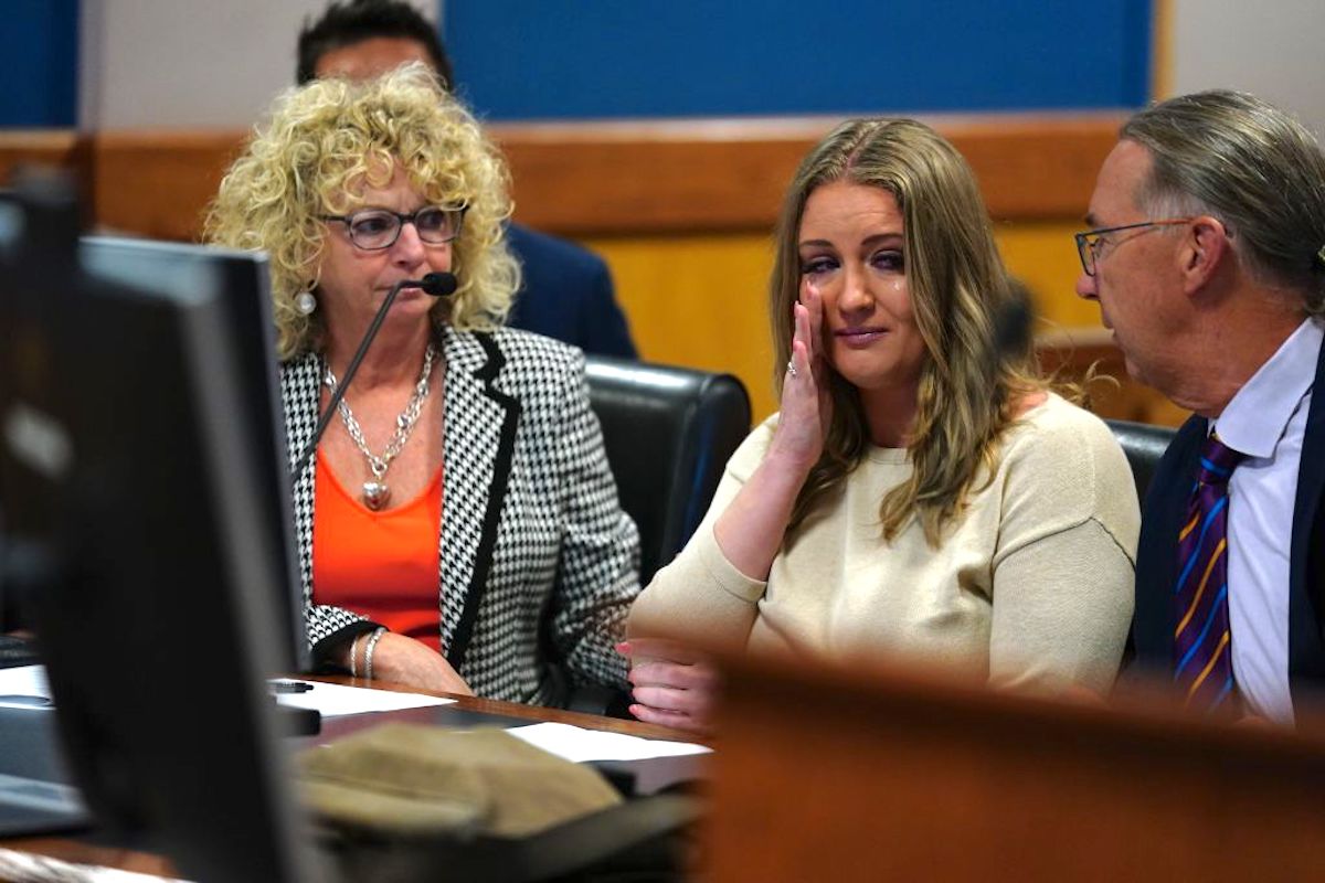 A white blond woman (Jenna Ellis) wipes away a tear while sitting in court.