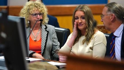 A white blond woman (Jenna Ellis) wipes away a tear while sitting in court.