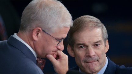 Jim Jordan bites his lip while leaning in to talk with another old white guy congressman.