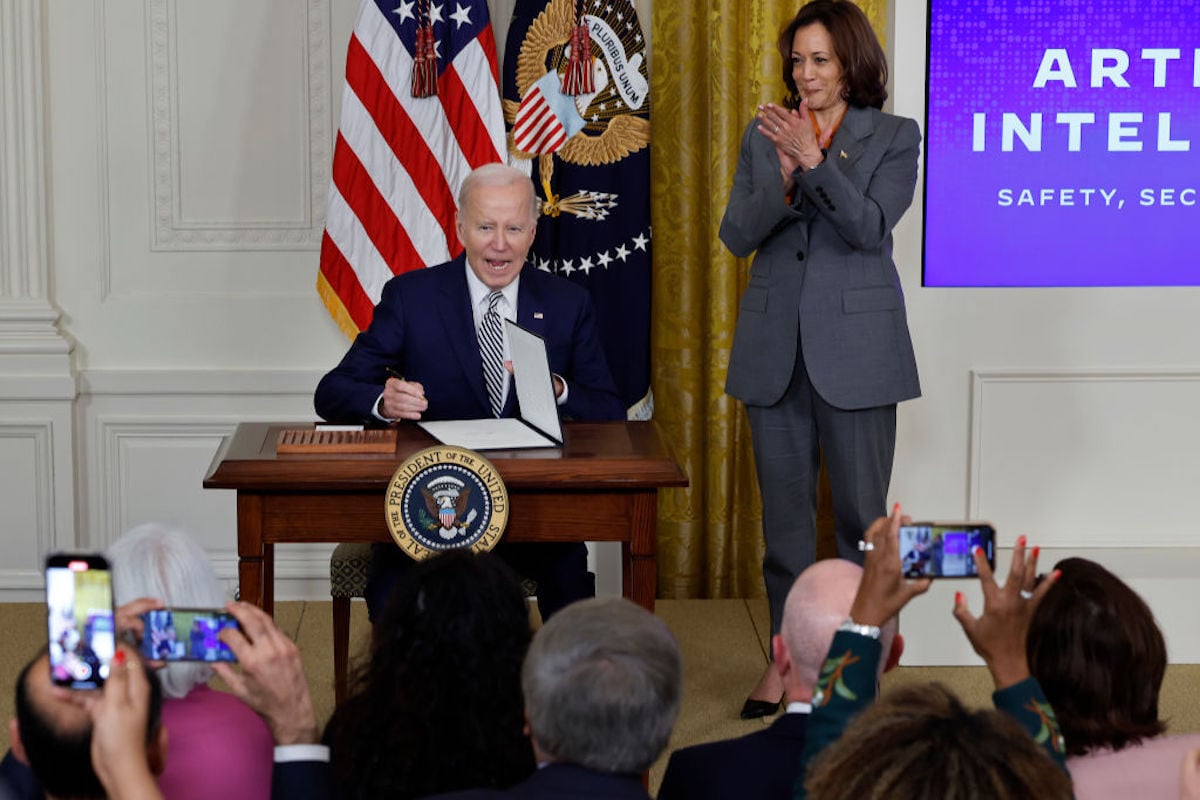 Vice President Kamala Harris (R) looks on as President Joe Biden signs a new executive order guiding his administration's approach to artificial intelligence