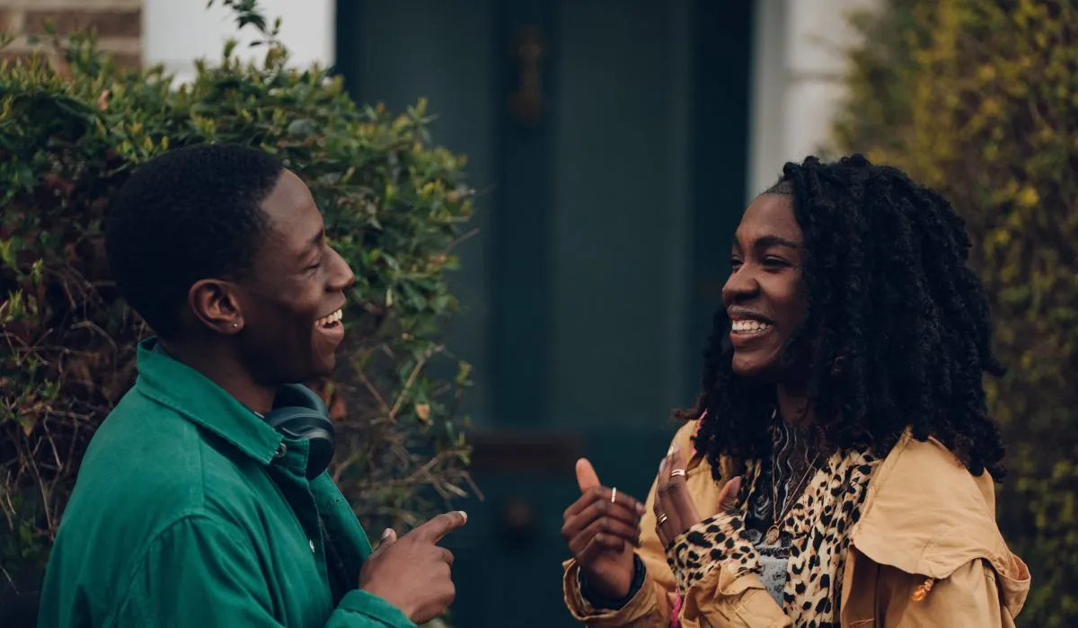 David Jonsson as Dom and Vivian Oparah Yas in 'Rye Lane' laughing with each other outside a house.