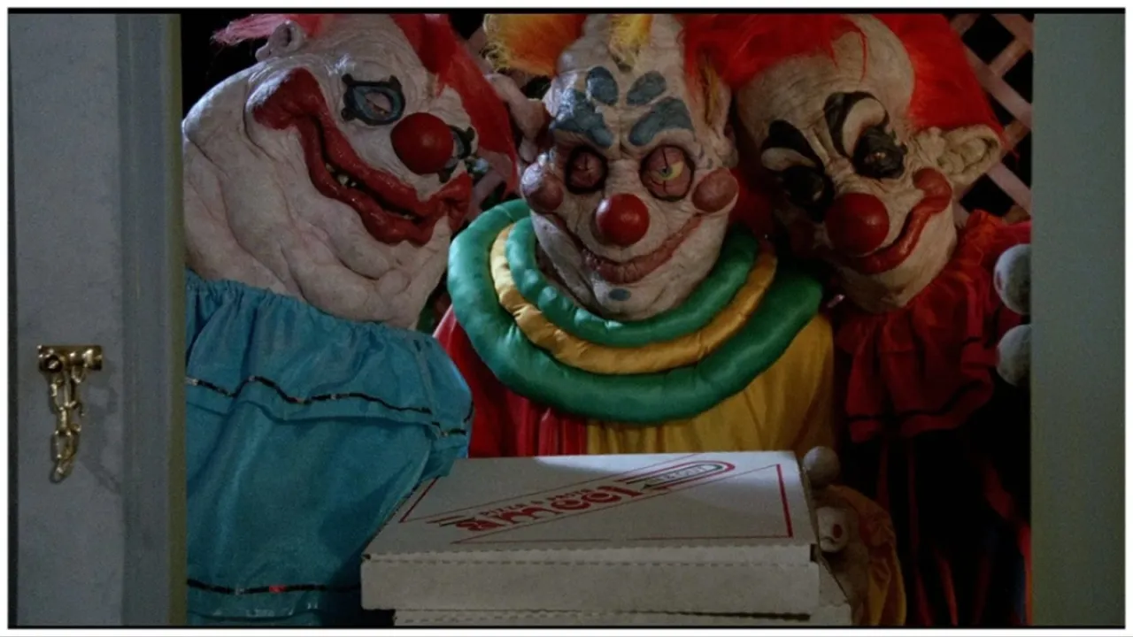 Three killer klowns from outer space stand at the door holding a pizza box in 'Killer Klowns from Outer Space'.
