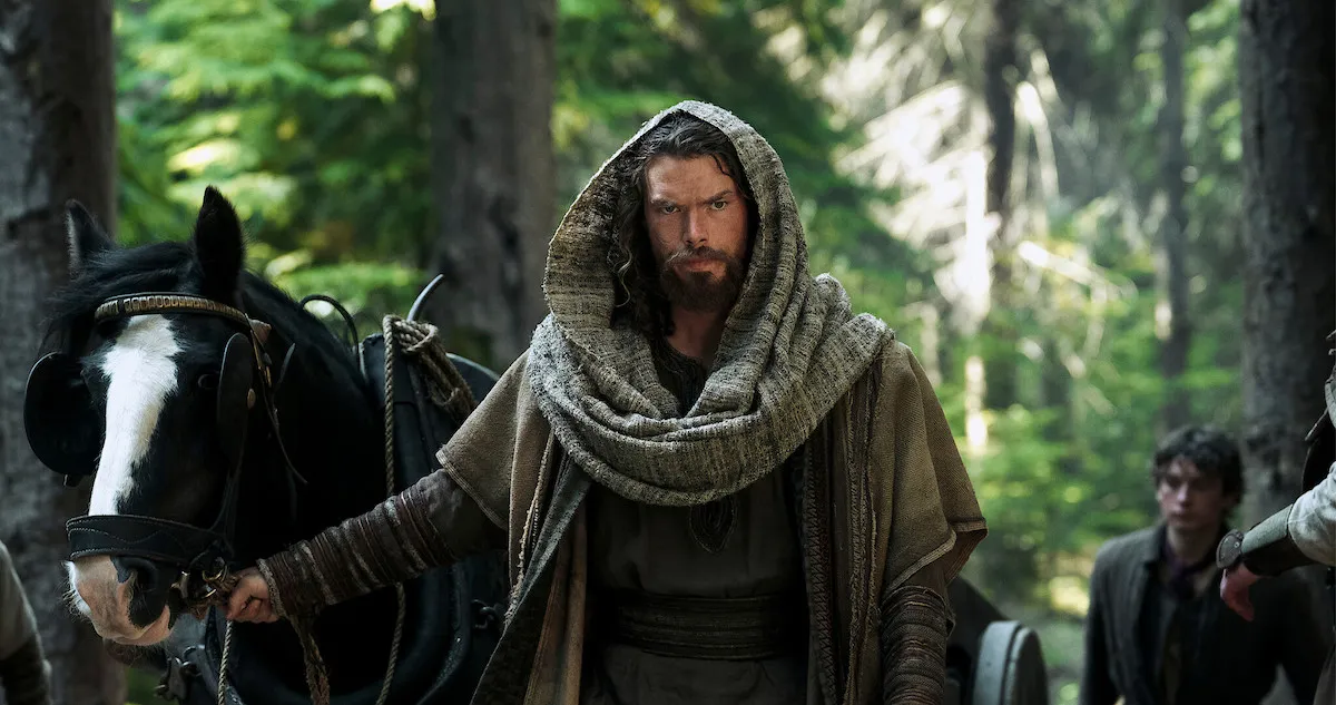 Sam Corlett as Leif Eriksson, wearing a cloak and leading a horse in a forest.