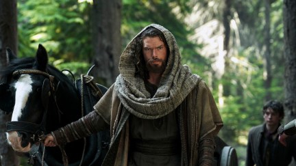 Sam Corlett as Leif Eriksson, wearing a cloak and leading a horse in a forest.