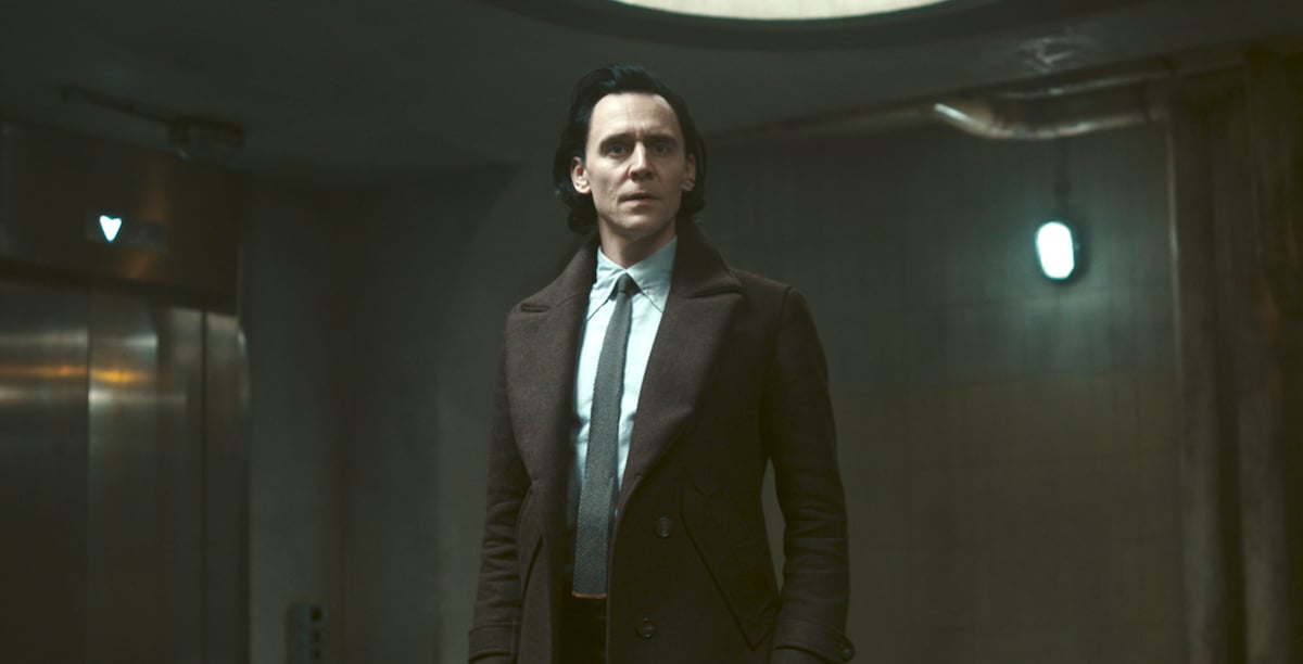 Loki stands in a dark hallway in the TVA, looking concerned.