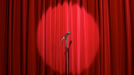 A microphone, in a spotlight, on an empty stage.