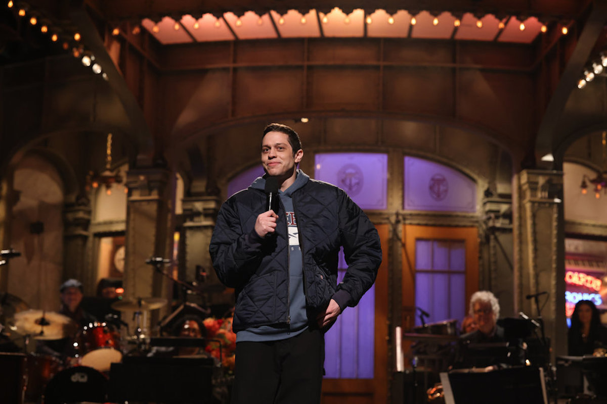 Pete Davidson stands on the SNL stage, holding a microphone.