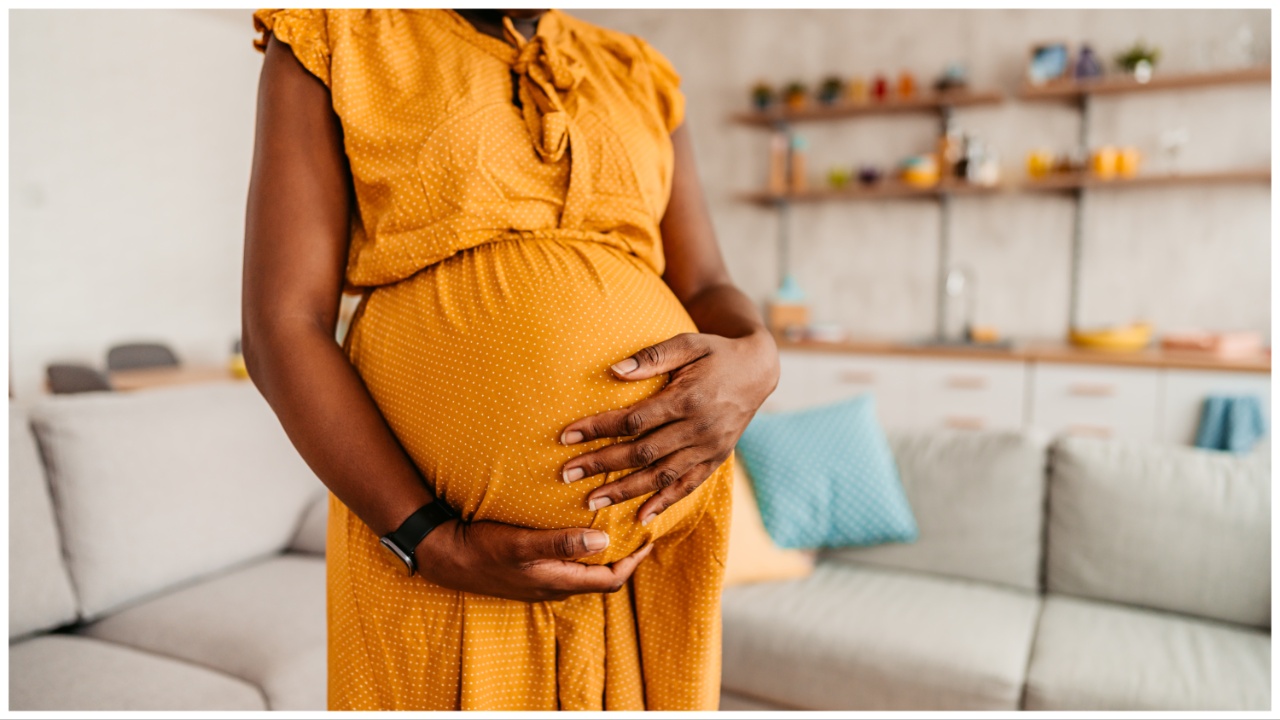 Portrait of beautiful pregnant black mother holding her pregnant belly at home. Close-up.