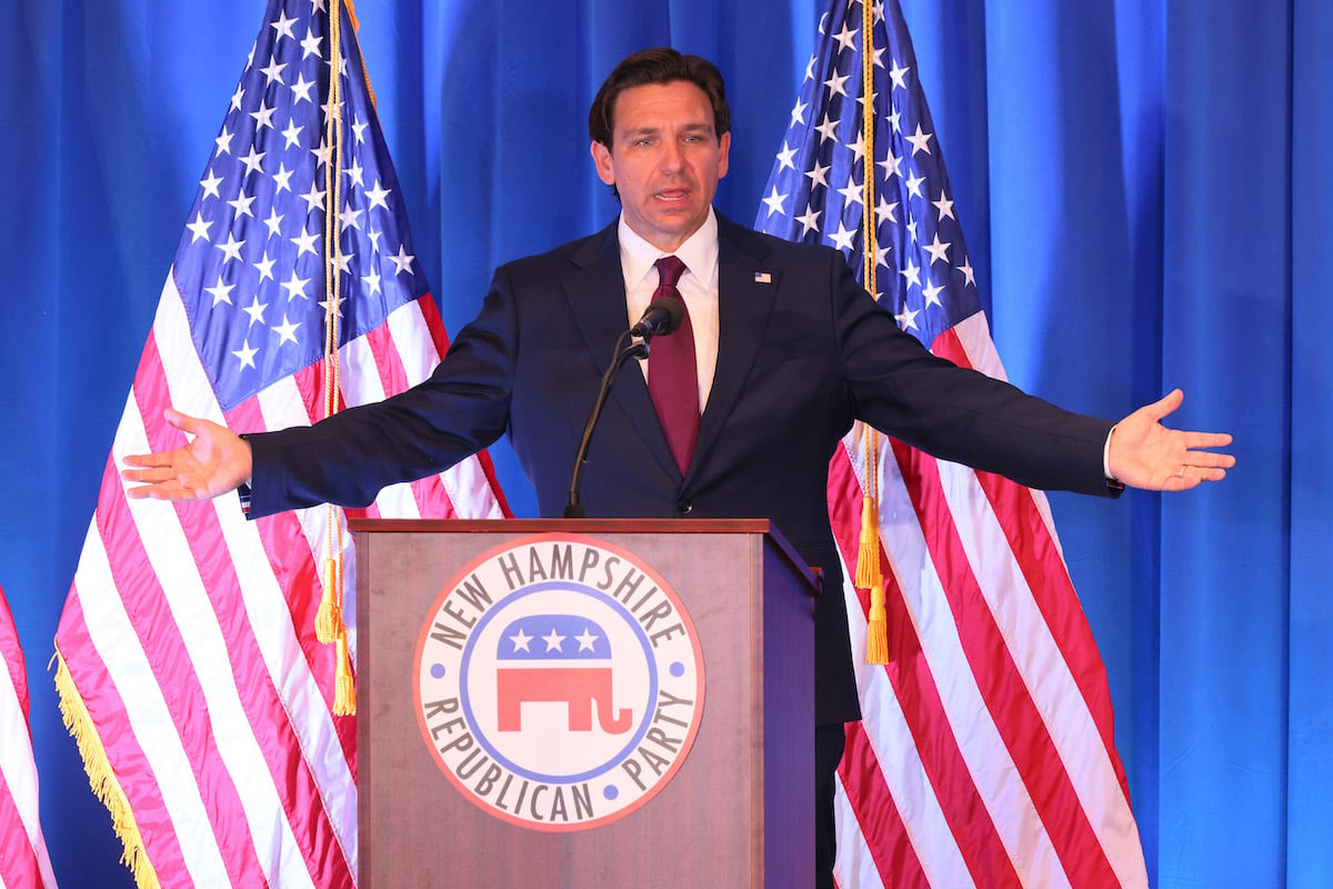 Ron Desantis speaks from a podium, his arms outstretched