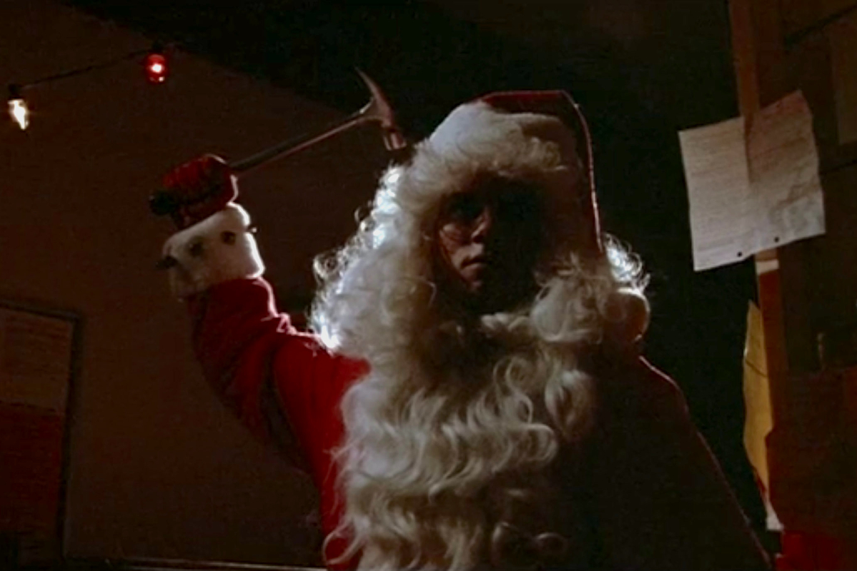 Still from Silent Night, Deadly Night; Robert Brian Wilson, dressed as Santa with the beard dropped under his chin raises an axe.