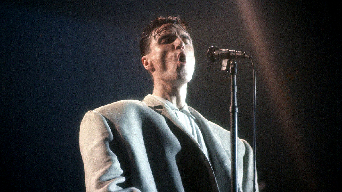 David Byrne wears his big suit while singing behind a microphone in Stop Making Sense.