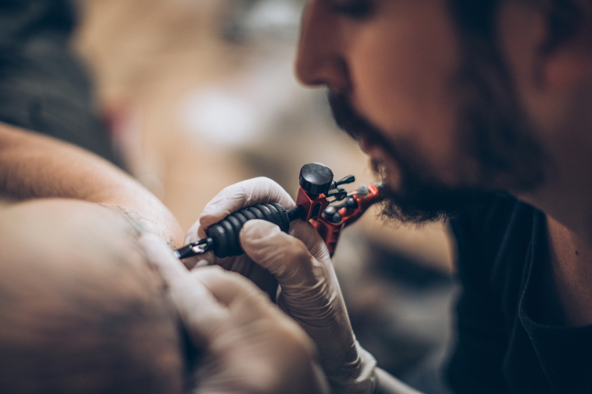Artist making tattoo on customer's hand in studio