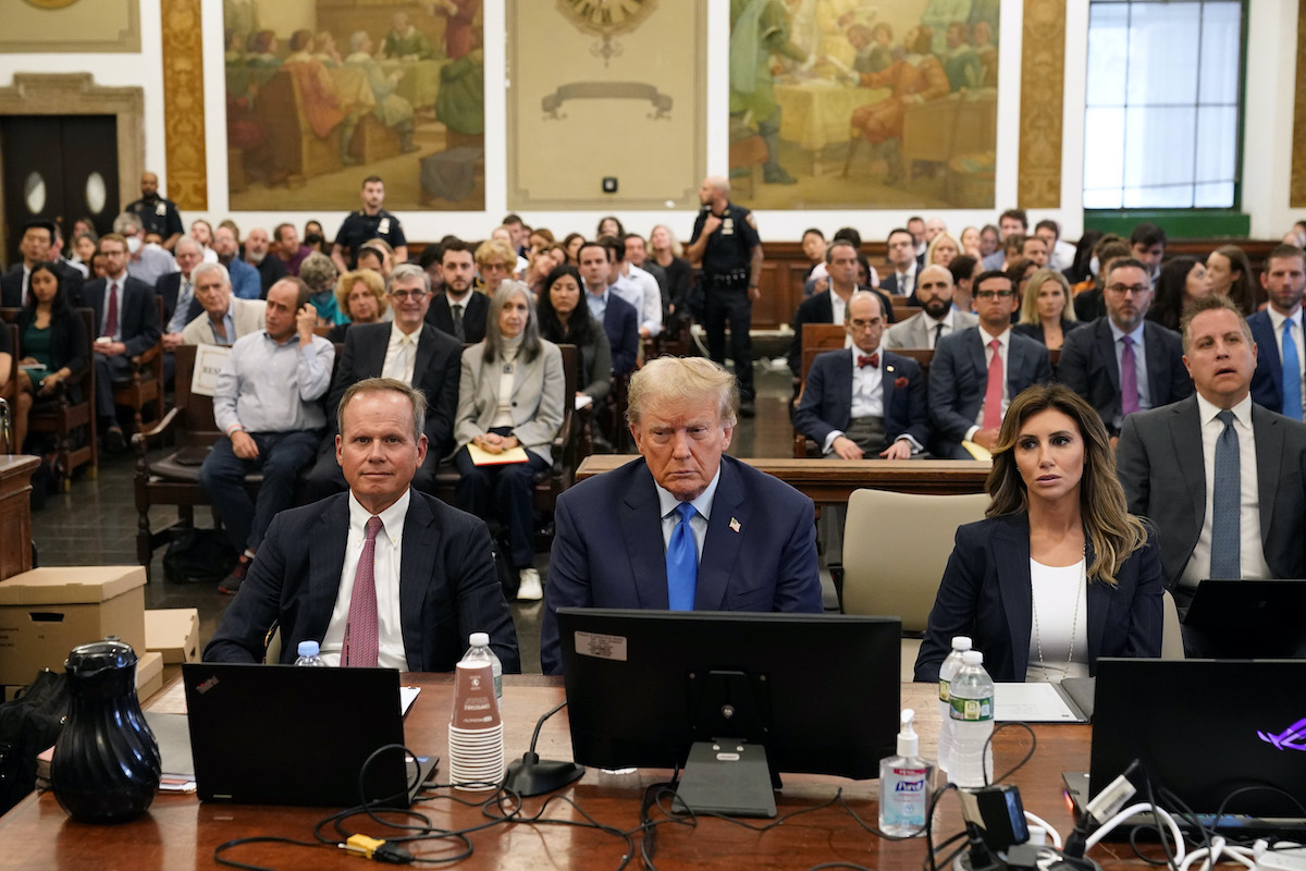 Donald Trump sits at the defendants' table in a courtroom, looking dejected.