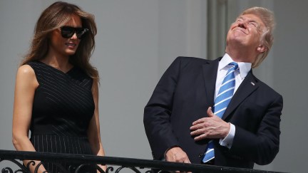Donald Trump stares at the sky, squinting, as Melania stands next to him wearing dark sunglasses.