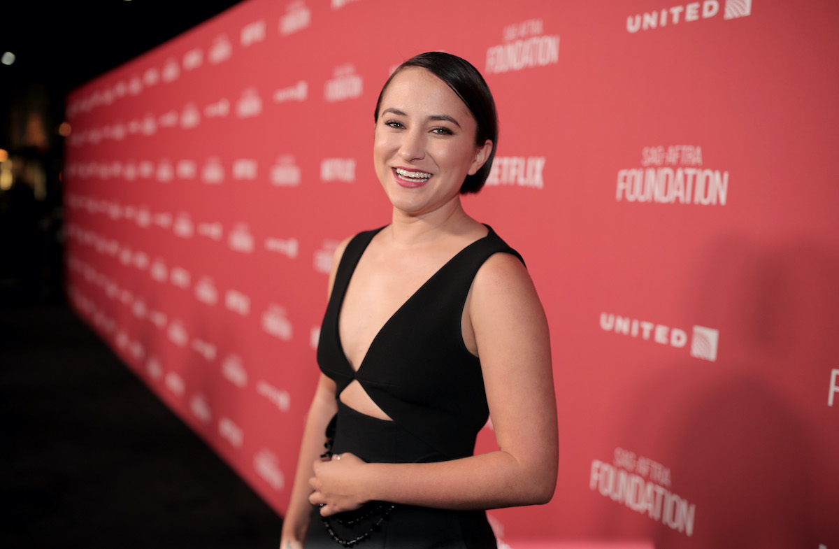 A young woman (Zelda Williams) on a red carpet, smiling at the camera.