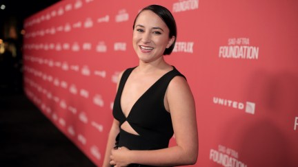 A young woman (Zelda Williams) on a red carpet, smiling at the camera.