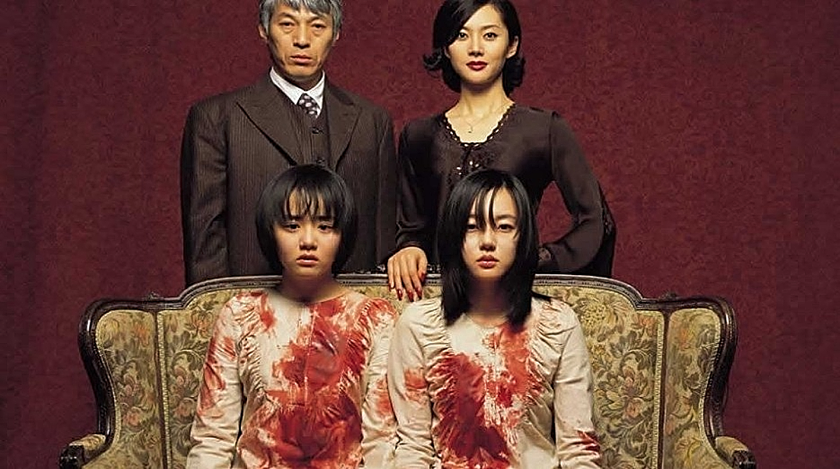 The cast of A Tale of Two Sisters, with two girls sitting down on a loveseat, completely covered in blood, their parents stood behind them.