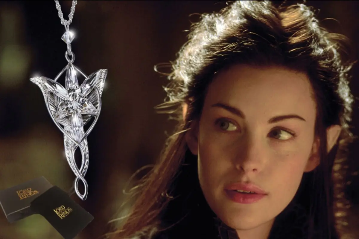 A photograph of a silver, art nouveau style pendant - the Evenstar. The background is a close up of actress Liv Tyler, a pale, dark haired woman.