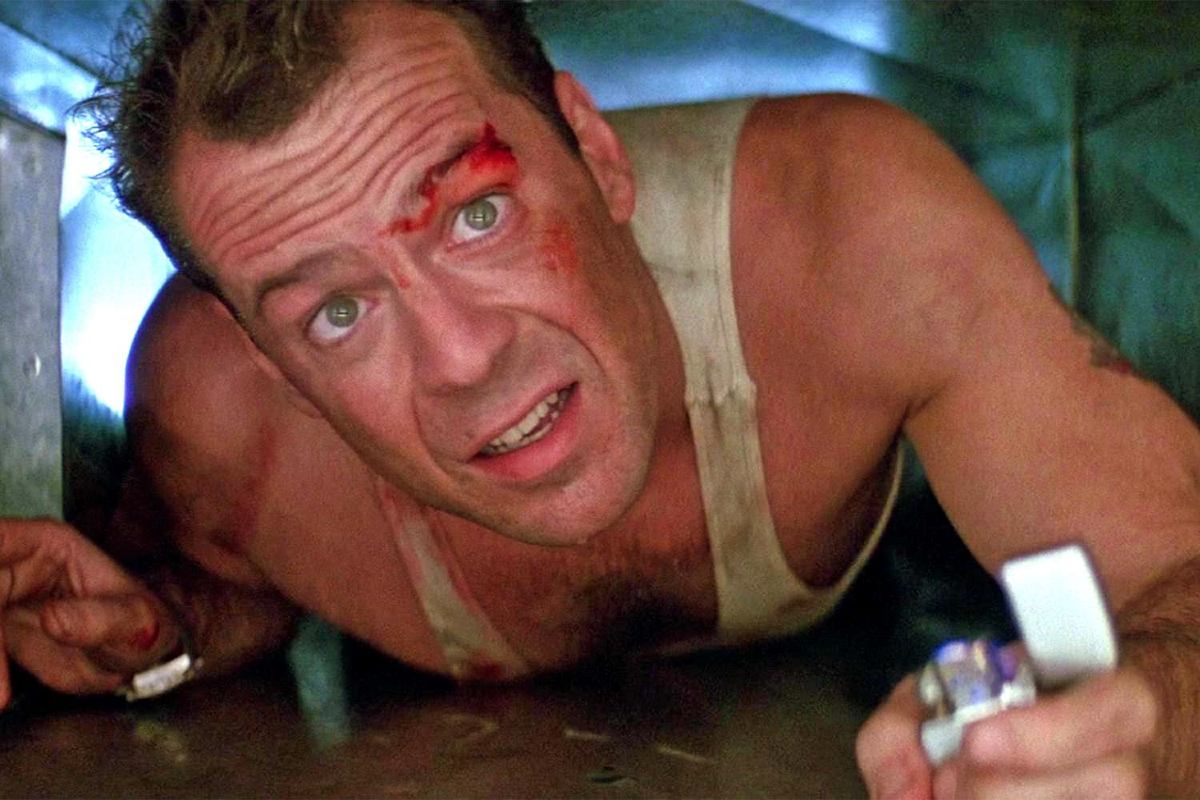 A white man with cuts on his face crawls through a vent in 'Die Hard.'