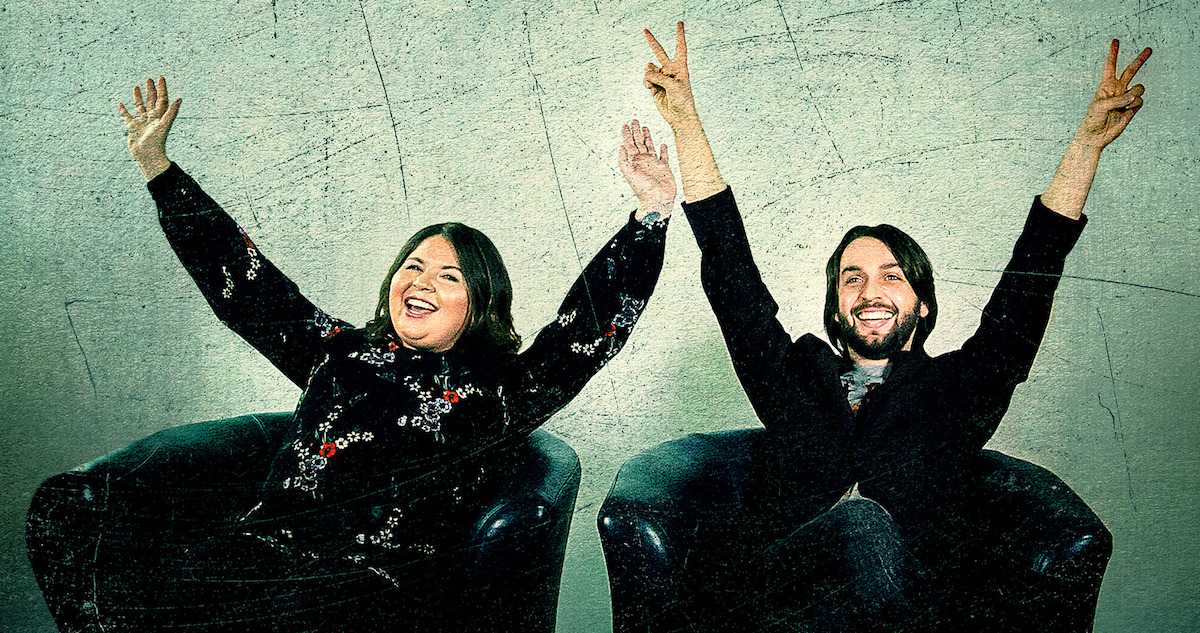 A white woman and white man sit in chairs with their arms raised and vapid smiles on their faces in 'Escaping Twin Flames.'