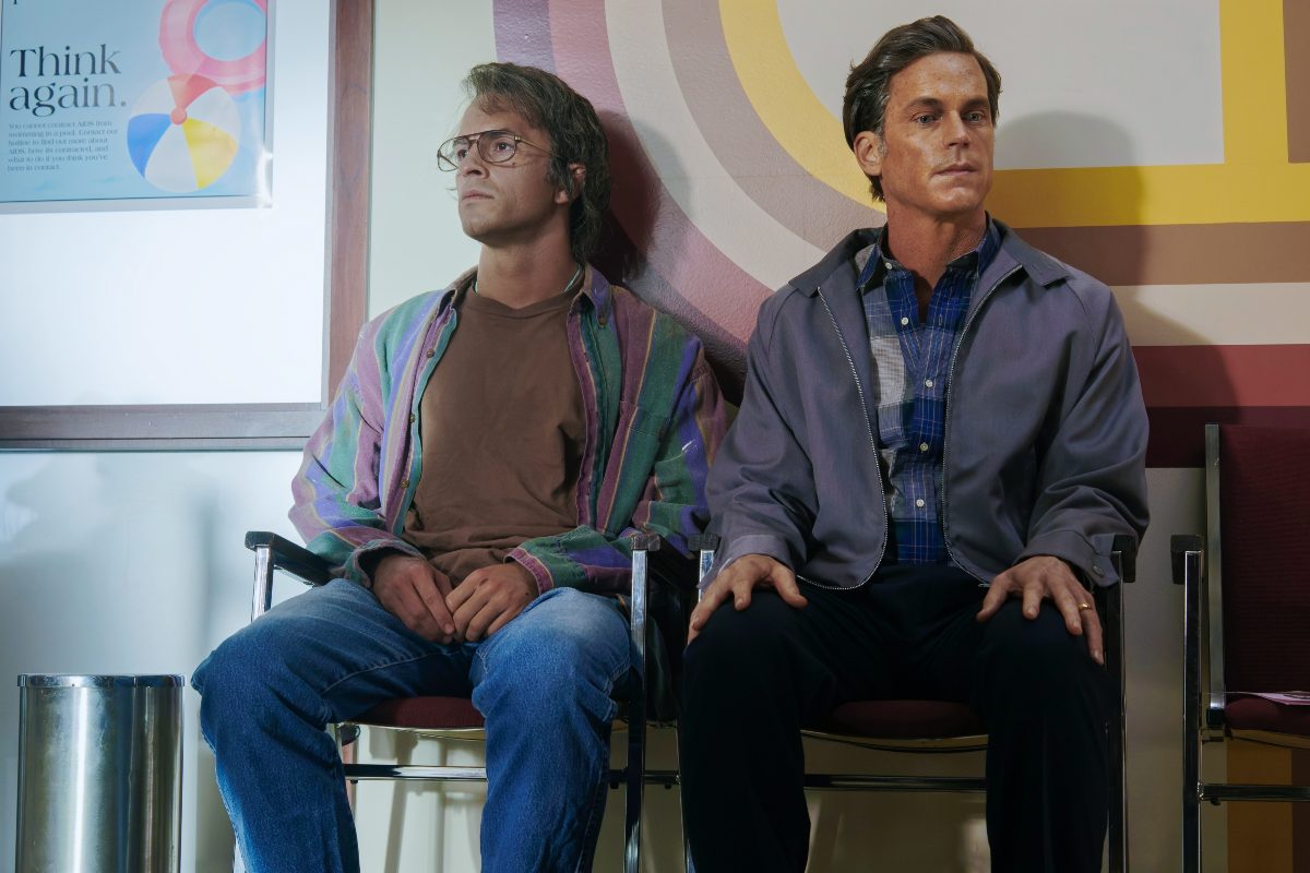 Two men (Jonathan Bailey and Matt Bomer) sit in an AIDS clinic waiting room in 'Fellow Travelers.'