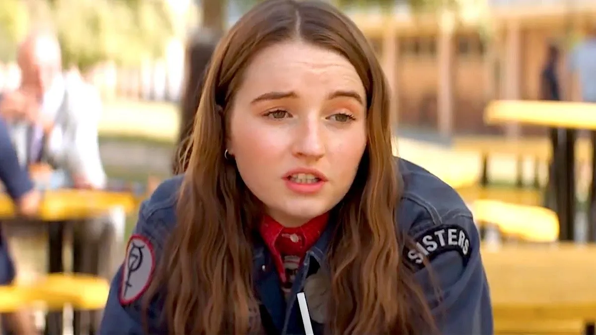 Image of Kaitlyn Dever in a scene from the film 'Booksmart.' She is a teenage girl with long brown hair wearing a blue jacket over a red polo shirt. She looks like she's making a sarcastic comment.
