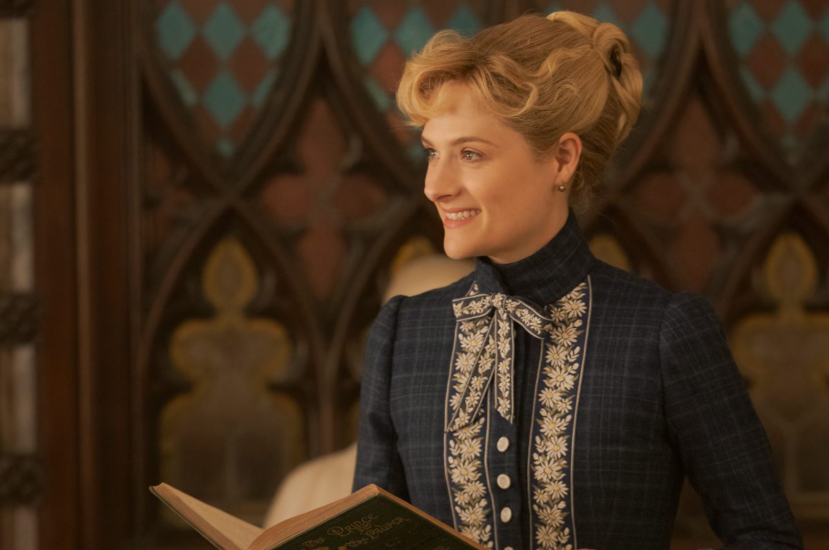 Louisa Jacobson as Marian Brook, a woman smiles while holding a book in 'The Gilded Age.'