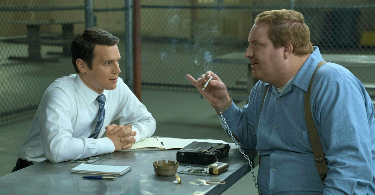 Holden Ford, wearing a shirt and tie, speaks to a felon across a table in Mindhunter.