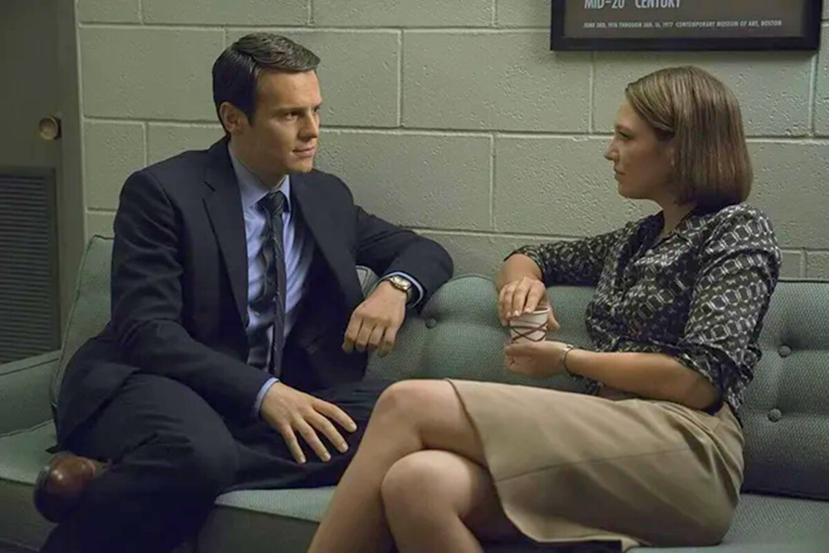 a man and a woman in business wear sit on a sofa looking at each other