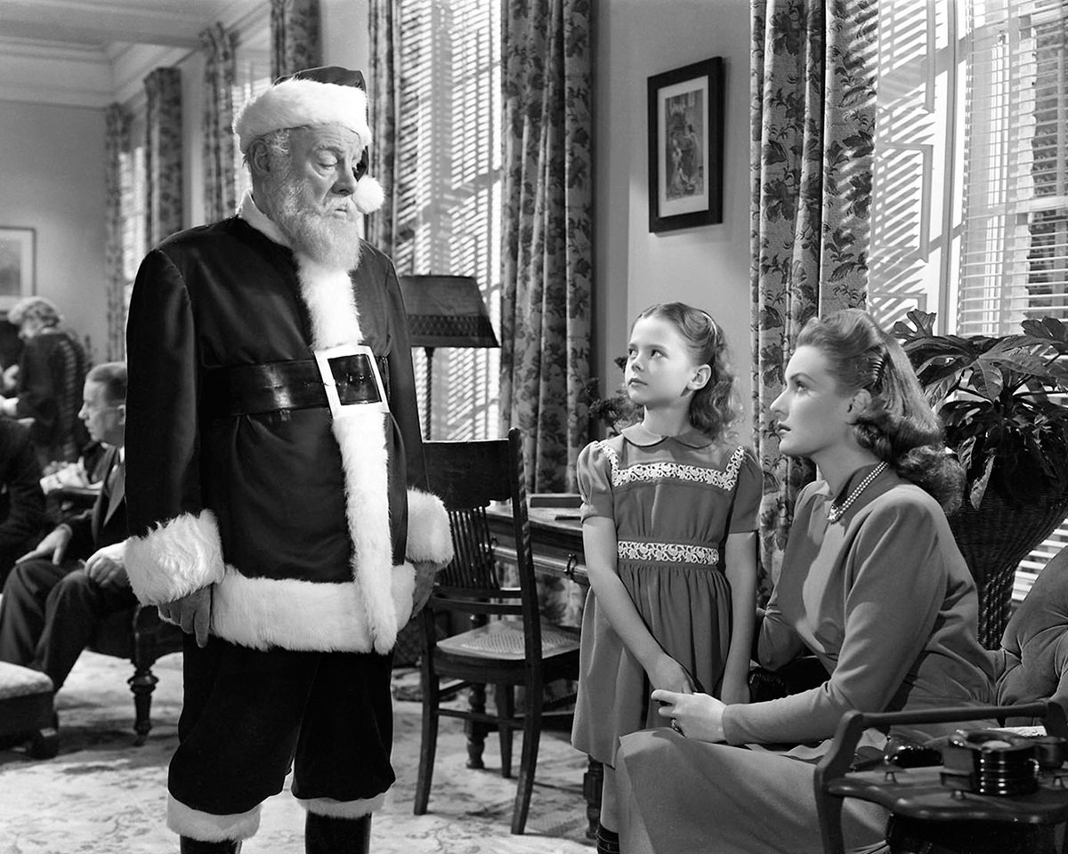 black and white still of Santa speaking with a mother and daughter