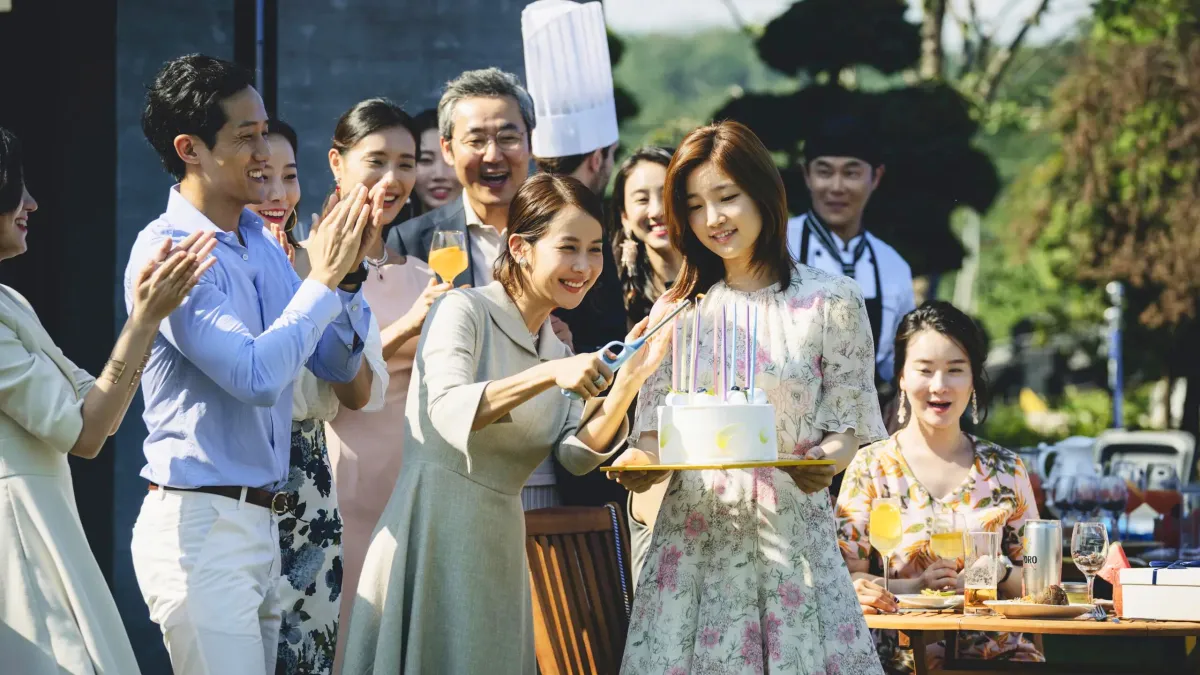 A group of South Korean party goers gather around a young woman holding a cake. Parasite movie.
