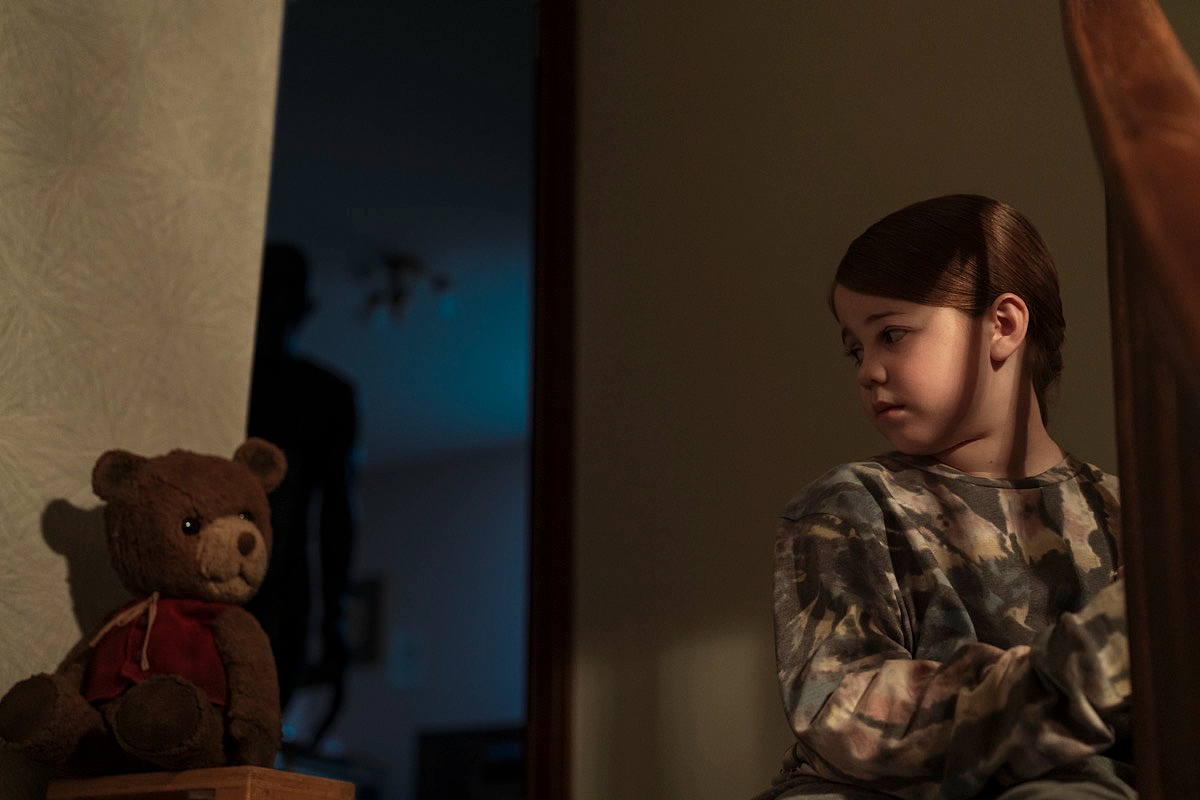 Pyper Braun in 'Imaginary,' a new horror movie from Blumhouse: a girl looks disconcertingly at a teddy bear while a dark figure lurks in the background