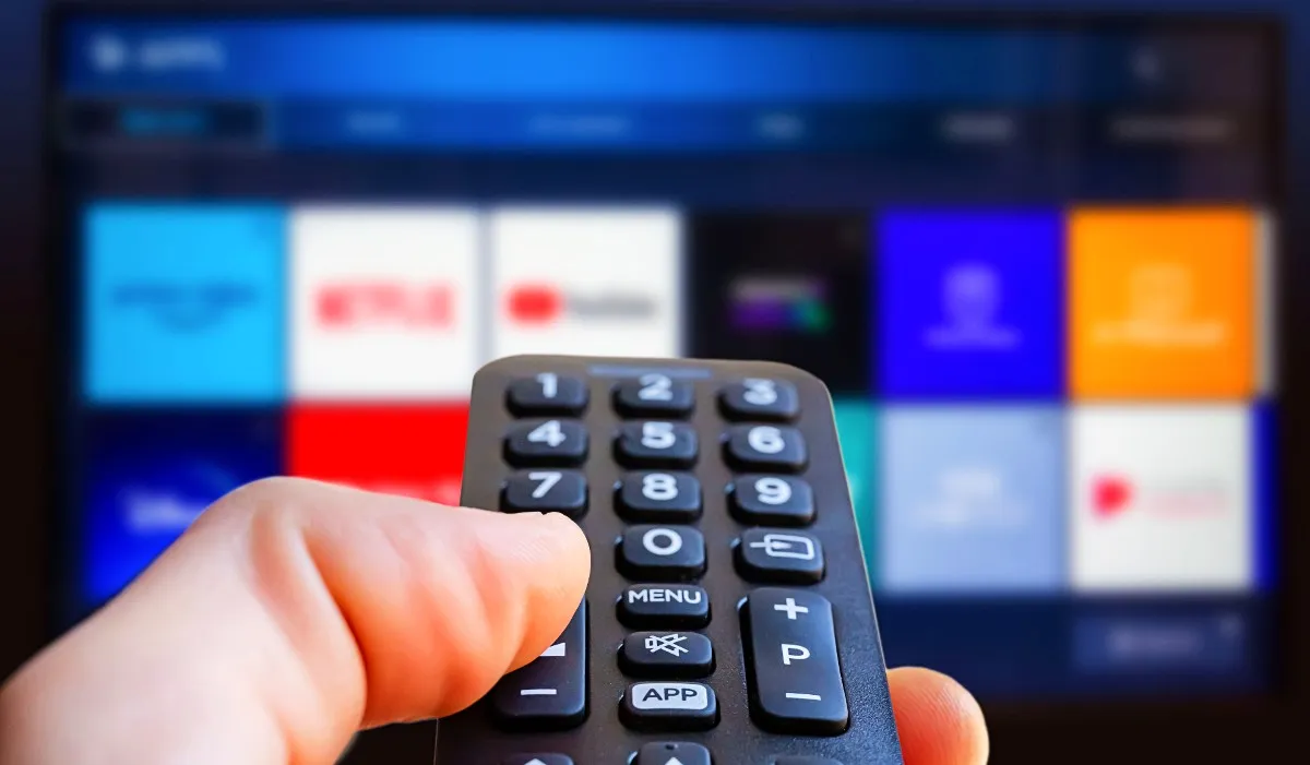 A TV remote in front of a blurred screen with streaming apps