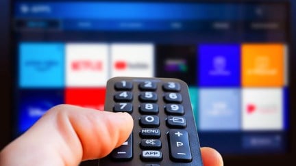 A TV remote in front of a blurred screen with streaming apps