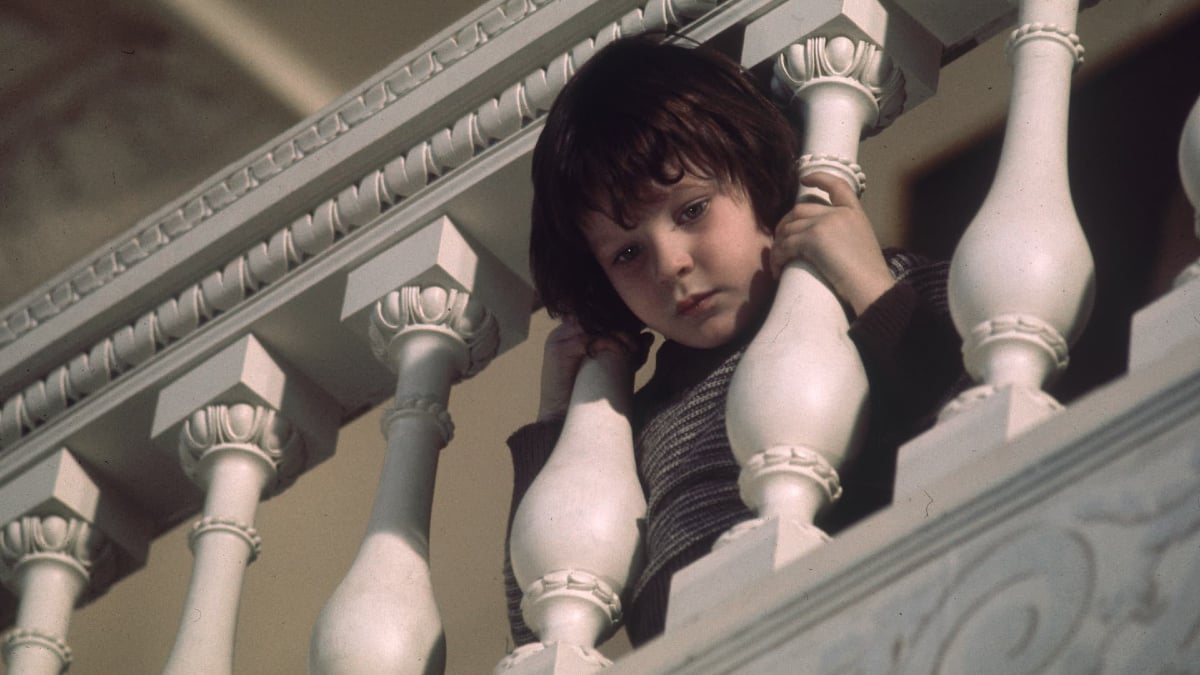 Damien peeks through the railing of some stairs in 'The Omen'