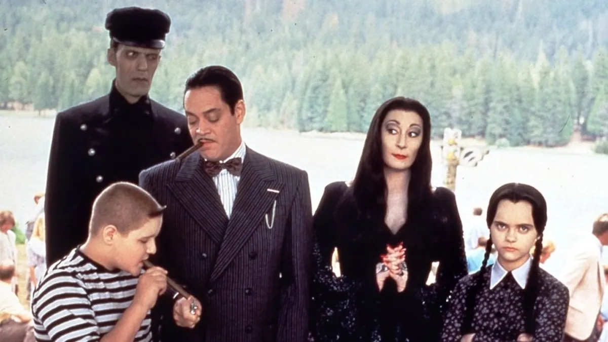 The cast of Addams Family Values stand in front of a lake.