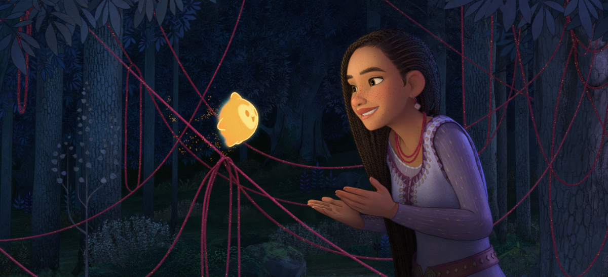 Asha smiles at Star in a dark forest with red yarn hanging from tree branches around them.