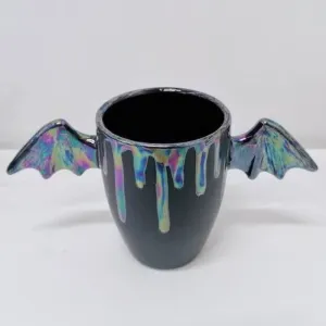 A mug with bat wings for handles and a pearlescent glaze on the rim and wings.